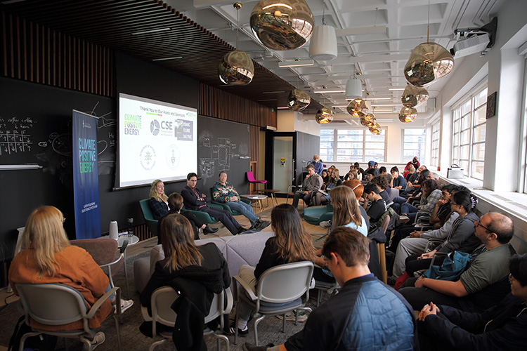 A large group of people in a room with three people presenting information.