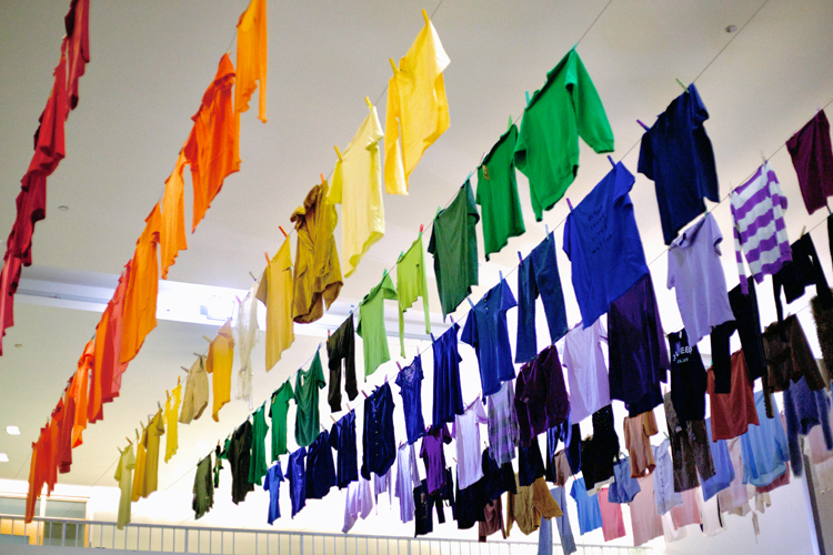 A rainbow of clothing hangs from a ceiling.