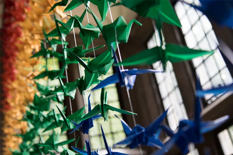 A close up image of rainbow paper cranes hanging in a large window at Hart House.