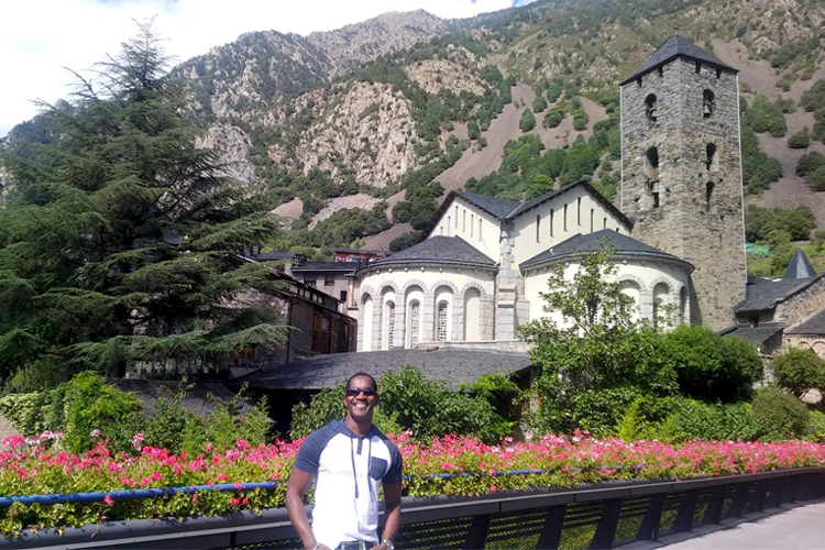 DeCoteau poses in Andorra La Vella a large building with mountains in the background.