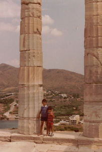 Dimitri Nakassis and his brother as children standing against an ancient pillar in Greece