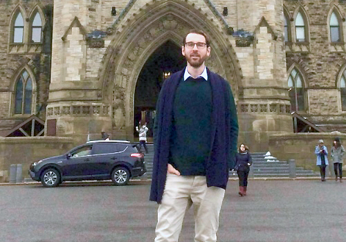 Donnelly standing in front of the large wood doors of Parliament's entrance.