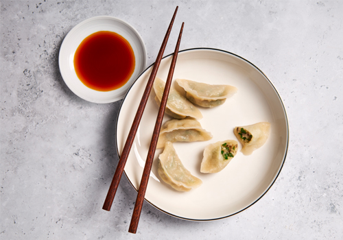Dumplings on a plate beside a small serving or sauce and chopsticks.