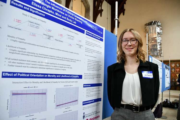 Elissa Chrapko standing in front of posters for their research.