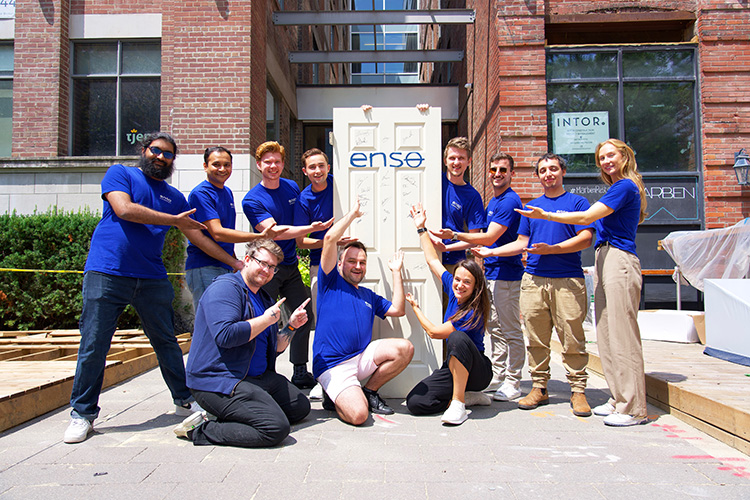 The Enso Connect team pose for a picture and hold a door with the Enso logo in blue.