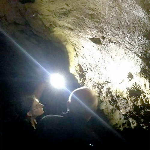 Sarah Ranlett stands in a cave with a flashlight conducting fieldwork.