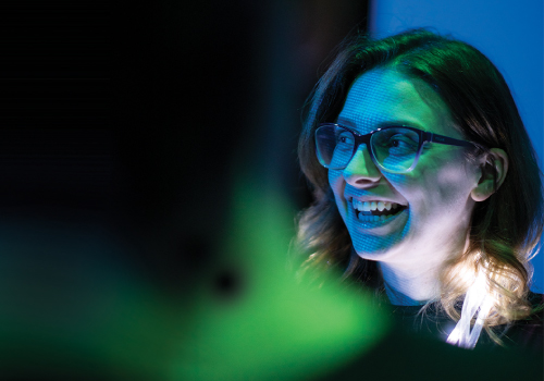 A person smiling with the reflection of a computer screen over her face.