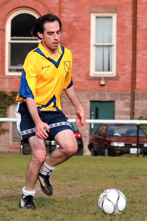 Paul Cohen in uniform kicking a soccer ball on a field
