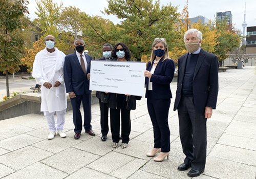 Bikila Award president Tessema Mulugeta, Bikila board member Behailu Atnafu, The Weeknd’s parents Samrawit Hailu and Walelegne Teshome, A&amp;S Dean Melanie Woodin and Professor Michael Gervers stand outside holding a large cheque on a beautiful fall day.