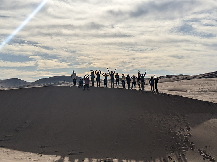 instructors and students standing with arms raised in joy on a sand dune