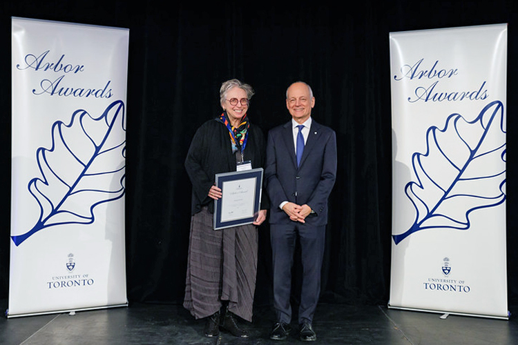Deanna Horton and U of T president Meric Gertler on stage holding a certificate in a frame.