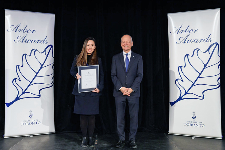 Han Yun (Jenny) Hsu and U of T president Meric Gertler on a stage holding a certificate in a frame.