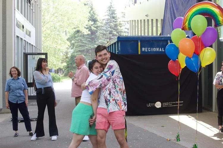 Two people hugging in beside colourful balloons