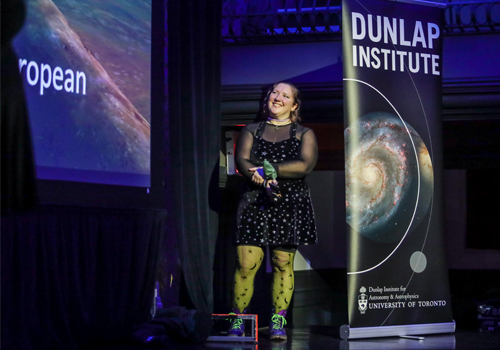 Ilana MacDonald presenting on a stage beside a Dunlap Institute banner.