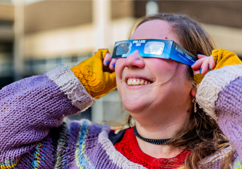 Ilana MacDonald smiling and wearing eclipse glasses.