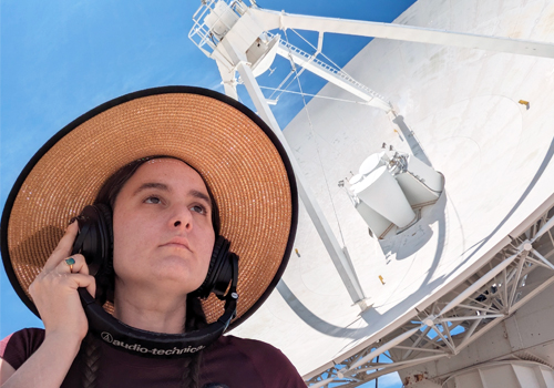 Kelly Lepo beside a satellite dish with headphones on.
