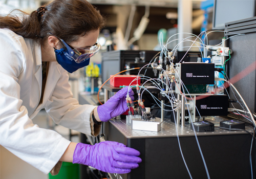 a gloved and masked woman in an advanced materials lab