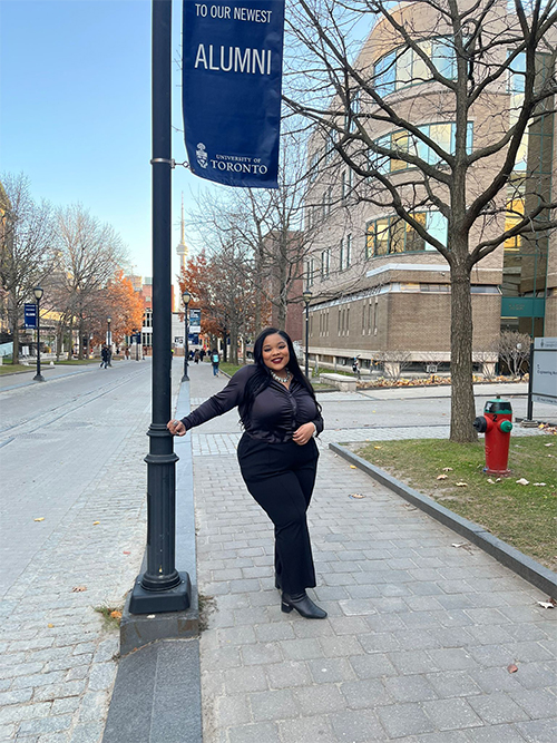 Lashae Watson on the U of T campus standing under an Alumni banner