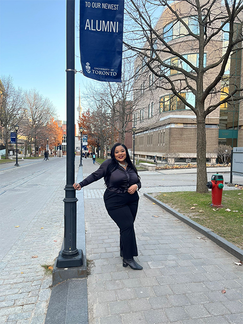 Lashae Watson on the U of T campus standing under an Alumni banner