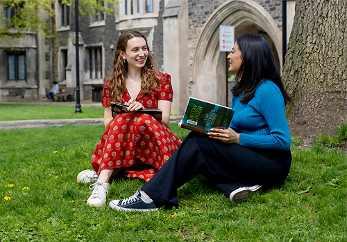 Lilly Flawn and Anuja Purohit sitting on grass outside studying.