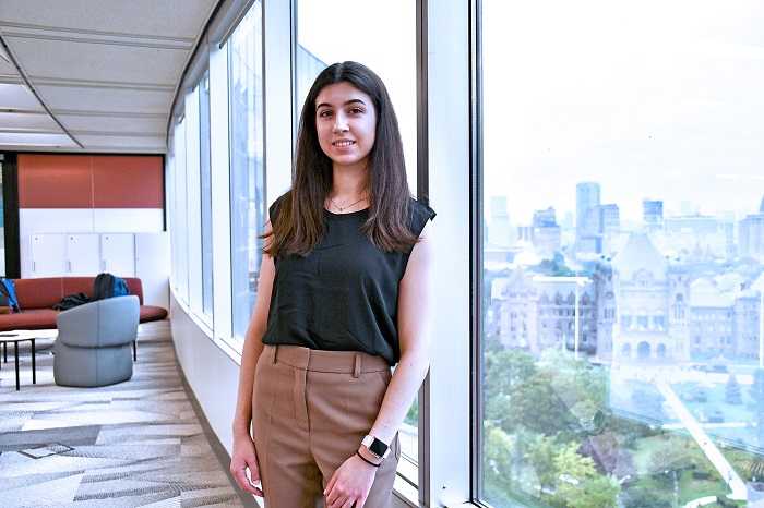 Student standing in front of a window in an office, Queen's Park building in the background