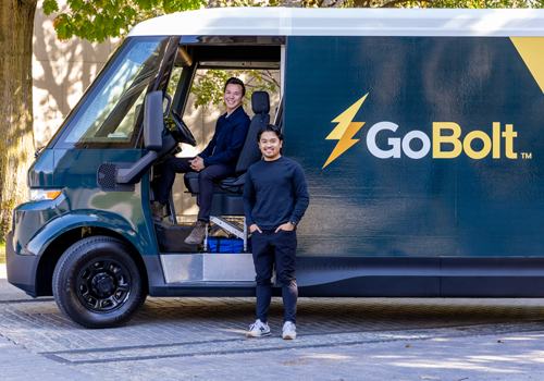 GoBolt co-founders Mark Ang sitting in the driver seat and Heindrik Bernabe standing beside a yellow and black truck that says, "Go Bolt."