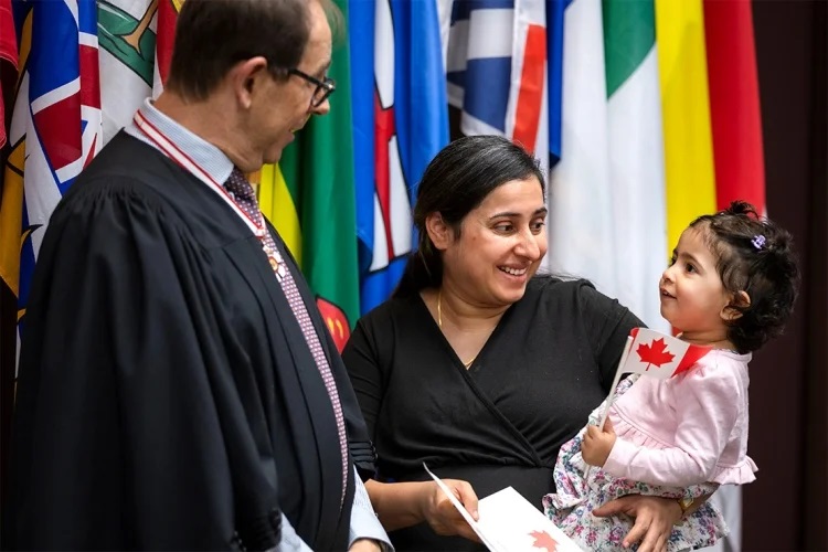 Mark Lautens laughs a woman holding a baby at a citizenship ceremony