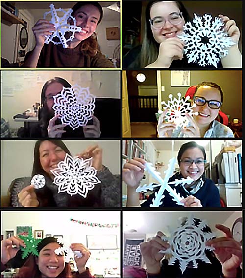 A group of people on video call showing paper snowflakes.