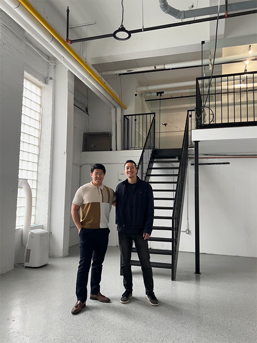 Charlie Hua and Frank Yu standing inside in front of a staircase.