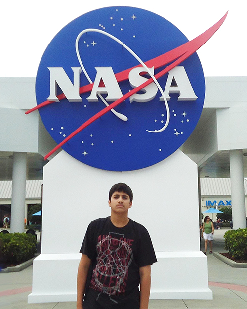 14-year-old Paracha standing in front of a blue and red NASA logo.
