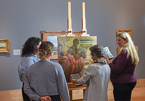 A group of people looking at a painting, the painting features a women's back.