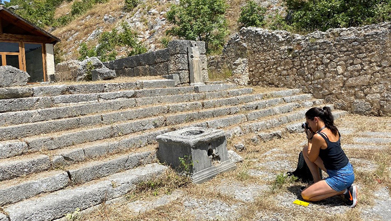 Claudia Paparella kneeling and taking a photo of an ancient ruin