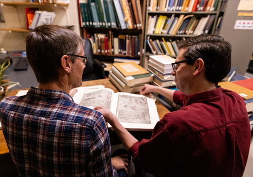 Two people sitting at a table reading a book.