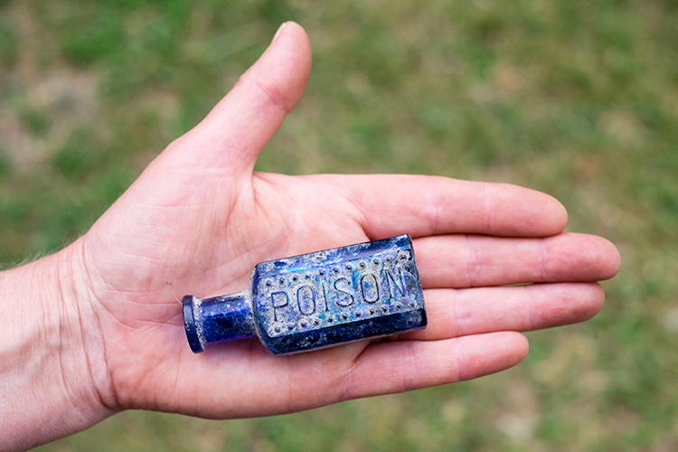 A hand holding a small blue bottle that says, "poison."