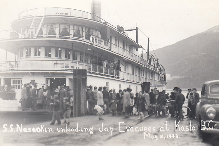 A black and white postcard of a ship and a large group of people.