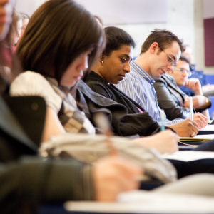 People sitting in a row, writing notes in a classroom.