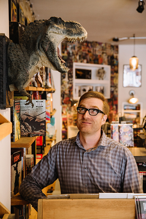 Ryan North sitting in his office with a dinosaur statue on the wall 