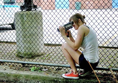 Sally Walker holding a camera on a sidewalk.