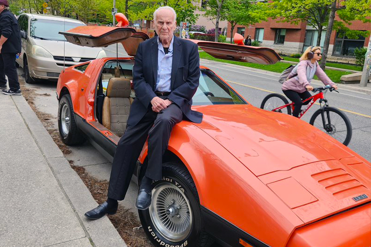 Malcolm Bricklin leaning against an orange gull-wing Bricklin SV-1.