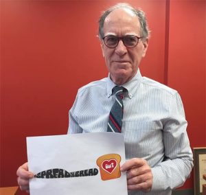 Dean of the Faculty of Arts &amp; Science David Cameron holding a sign for with a slide of bread and a butter knife to support #SpreadTheBreadUofT campaign.