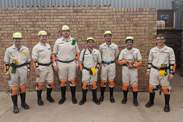 Students pose in front of a brick wall, ready to descend into the Moab Khotsong gold mine.