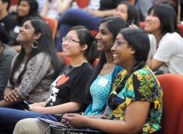 A group of students sit and smile within a lecture hall.