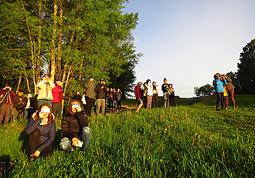 A group of people with viewing glasses on to see an eclipse in a field.