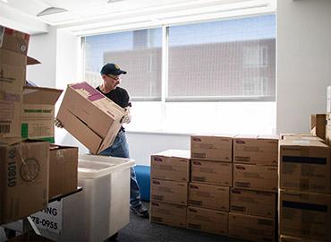 A worker lifts boxes of personal protective equipment supplies amidst stacks of other boxes