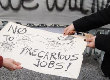 A sign reads, &amp;quot;No to precarious jobs&amp;quot;. 