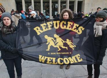 Three protesters holding a banner that says &amp;quot;Refugees Welcome&amp;quot;