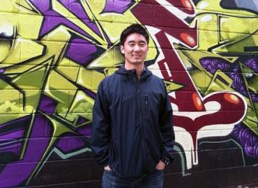 Jooyoung Lee standing in front of a wall with colourful graffiti on it