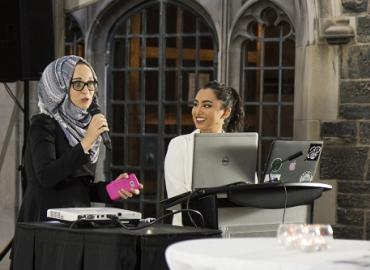 Syrian newcomer Hanen Nanaa speaks on a microphone next to U of T student Muriam Fancy