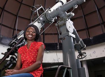 Margaret Ikape posing in front of a telescope
