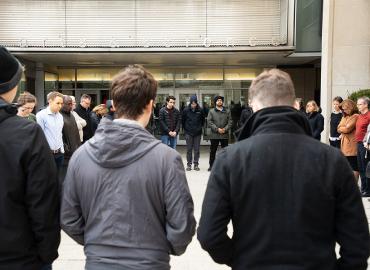 A group of people gather for a moment of silence in front of Sid Smith.